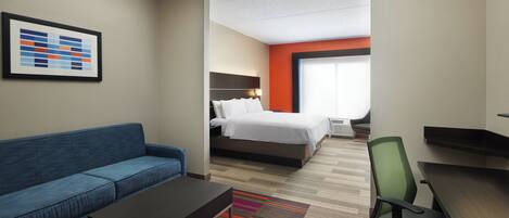 A hotel room with a blue sofa, a bed with white bedding, a desk, and a colorful striped rug.