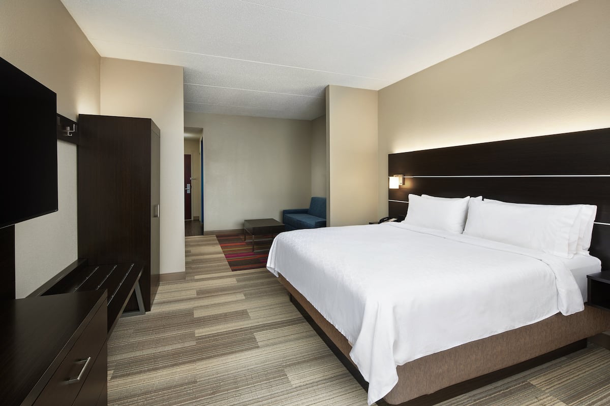 A modern hotel room with a large bed, a flat-screen TV, a desk, and a chair.