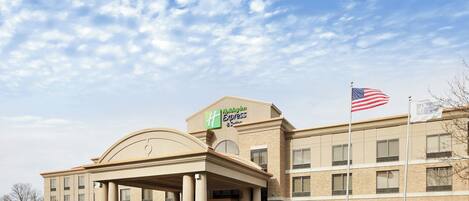 A Holiday Inn Express hotel with a prominent American flag, a covered entrance, and a parking lot.