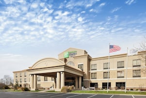 Un hotel Holiday Inn Express con una destacada bandera estadounidense, una entrada cubierta y un estacionamiento.