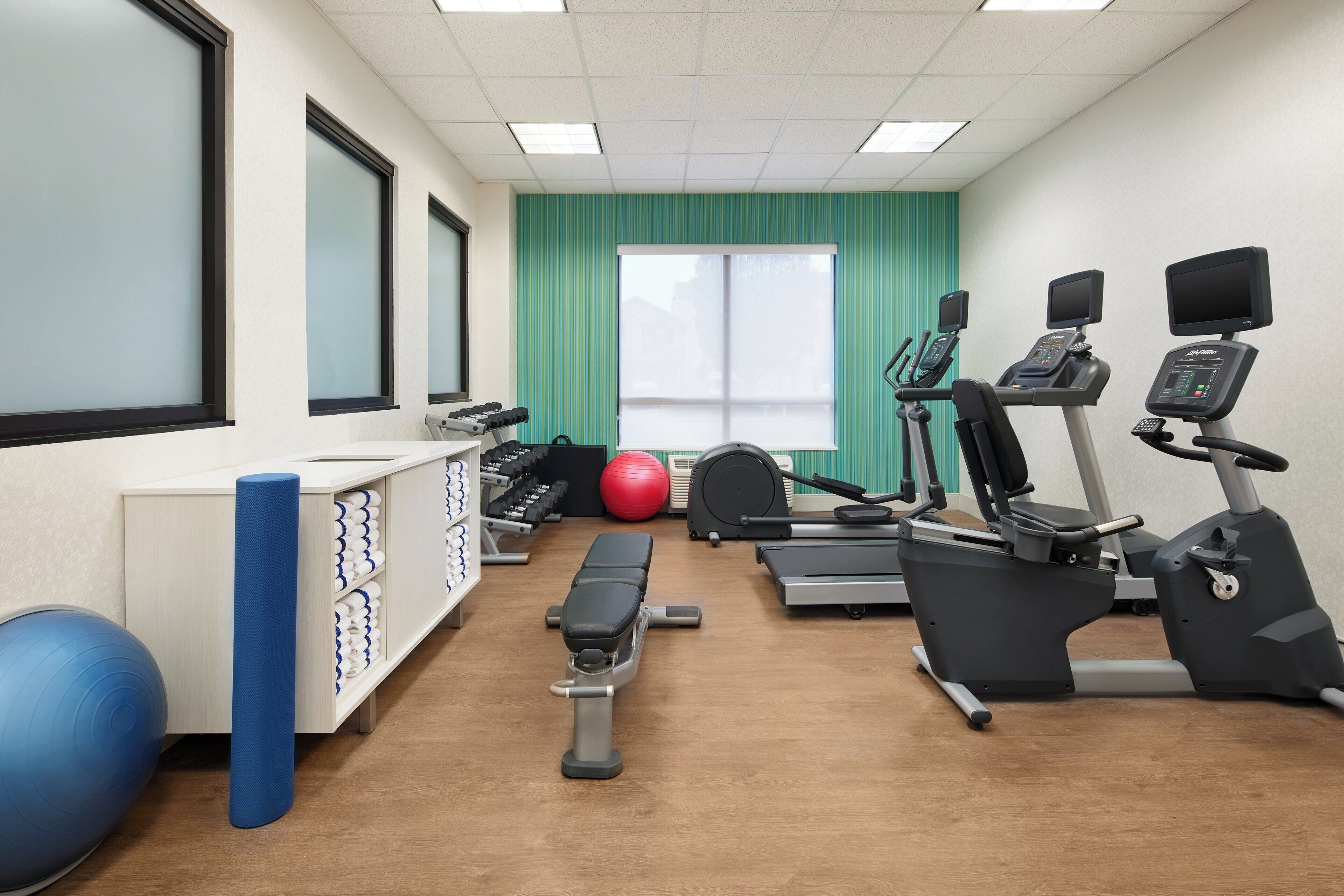 A fitness center with exercise equipment, a bench, and a wall-mounted rack with towels.