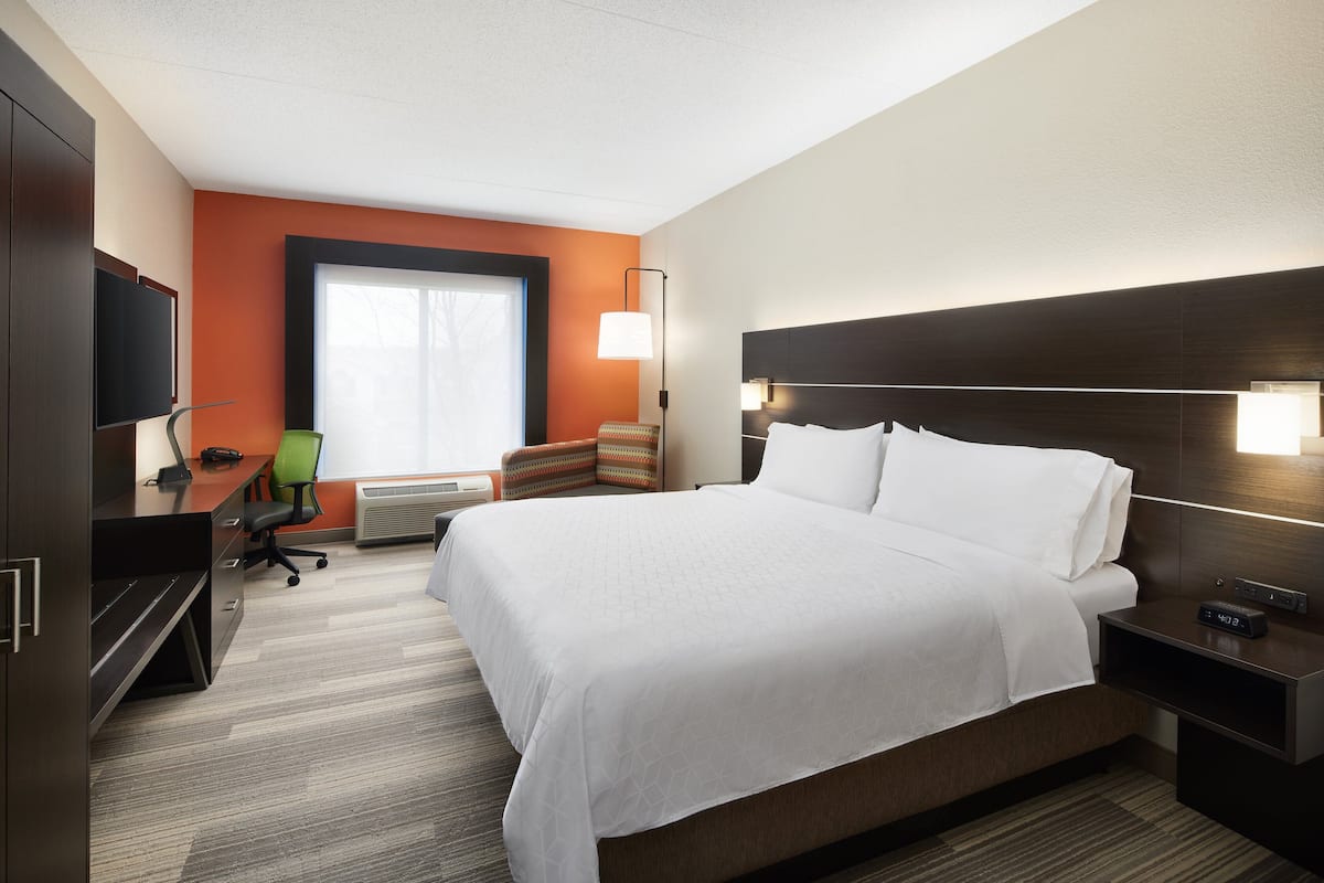 A hotel room with a large bed, a desk with a chair, a television, and a window with blinds.