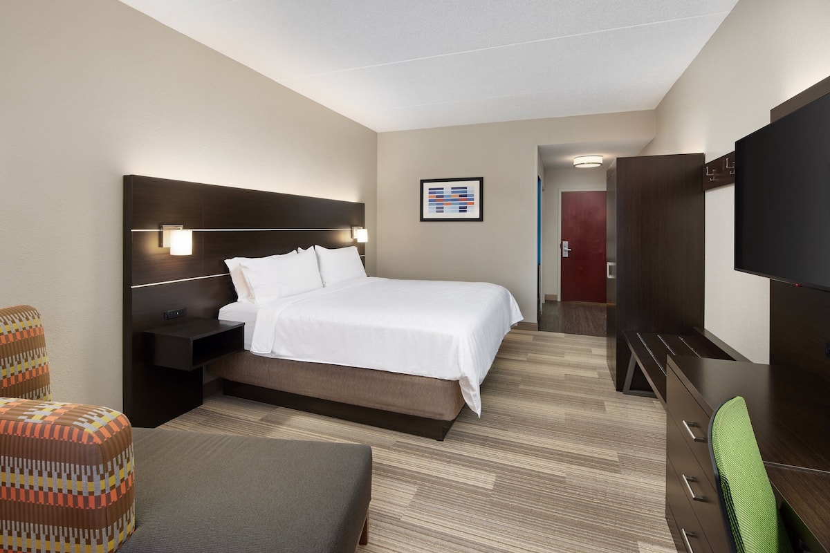 A hotel room with a large bed, bedside tables, a TV, and a seating area.