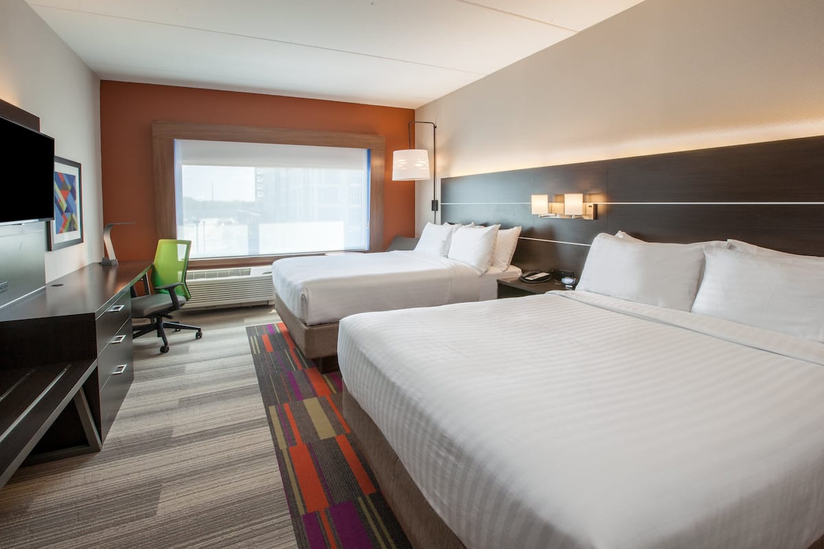 A hotel room with two beds, a desk, a chair, a TV, and a large window.