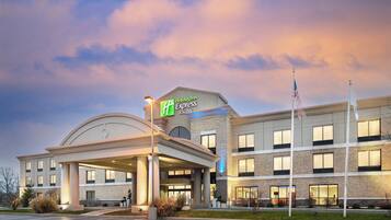 Ett Holiday Inn Express & Suites-hotell med en ingång som är skyddad från väder och vind, en parkeringsplats och en flaggstång.