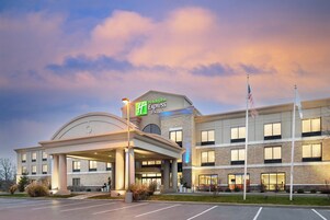 A Holiday Inn Express & Suites hotel with a covered entrance, a parking lot, and a flagpole.