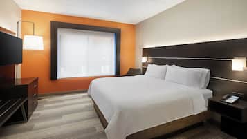 Une chambre d’hôtel avec un grand lit, un téléviseur posé sur une commode et une fenêtre équipée de stores.