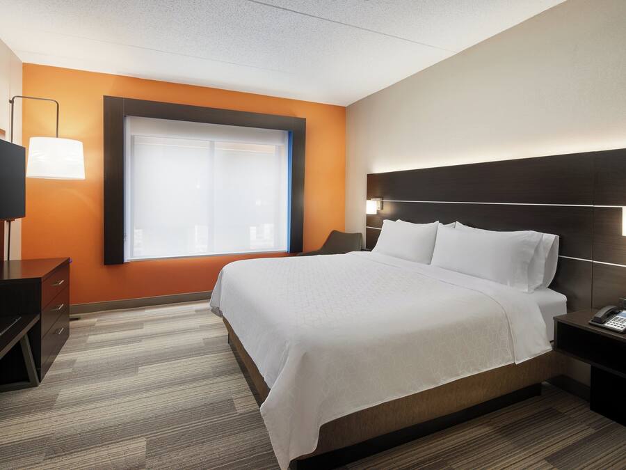 Une chambre d’hôtel avec un grand lit, un téléviseur posé sur une commode et une fenêtre équipée de stores.