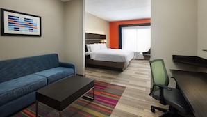 A hotel room with a blue sofa, a bed with white bedding, a desk with a chair, and a colorful striped rug.