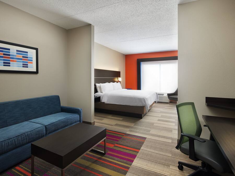 Une chambre d’hôtel avec un canapé bleu, un lit avec une literie blanche, un bureau avec une chaise et un tapis rayé aux couleurs vives.