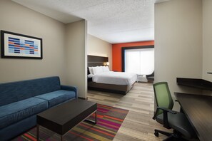 A hotel room with a blue sofa, a bed with white bedding, a desk with a chair, and a colorful striped rug. - Holiday Inn Express & Suites Seymour by IHG (Seymour)