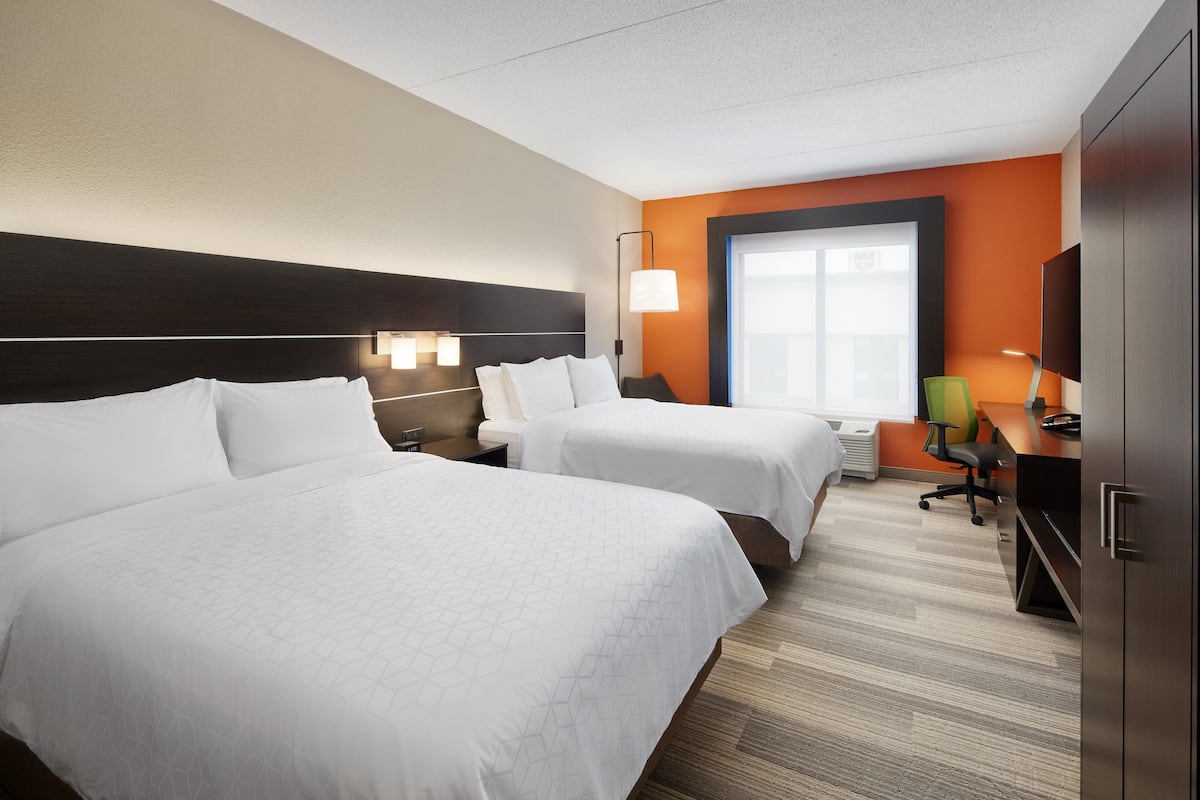 A hotel room with two beds, a desk, a chair, a TV, and a window.
