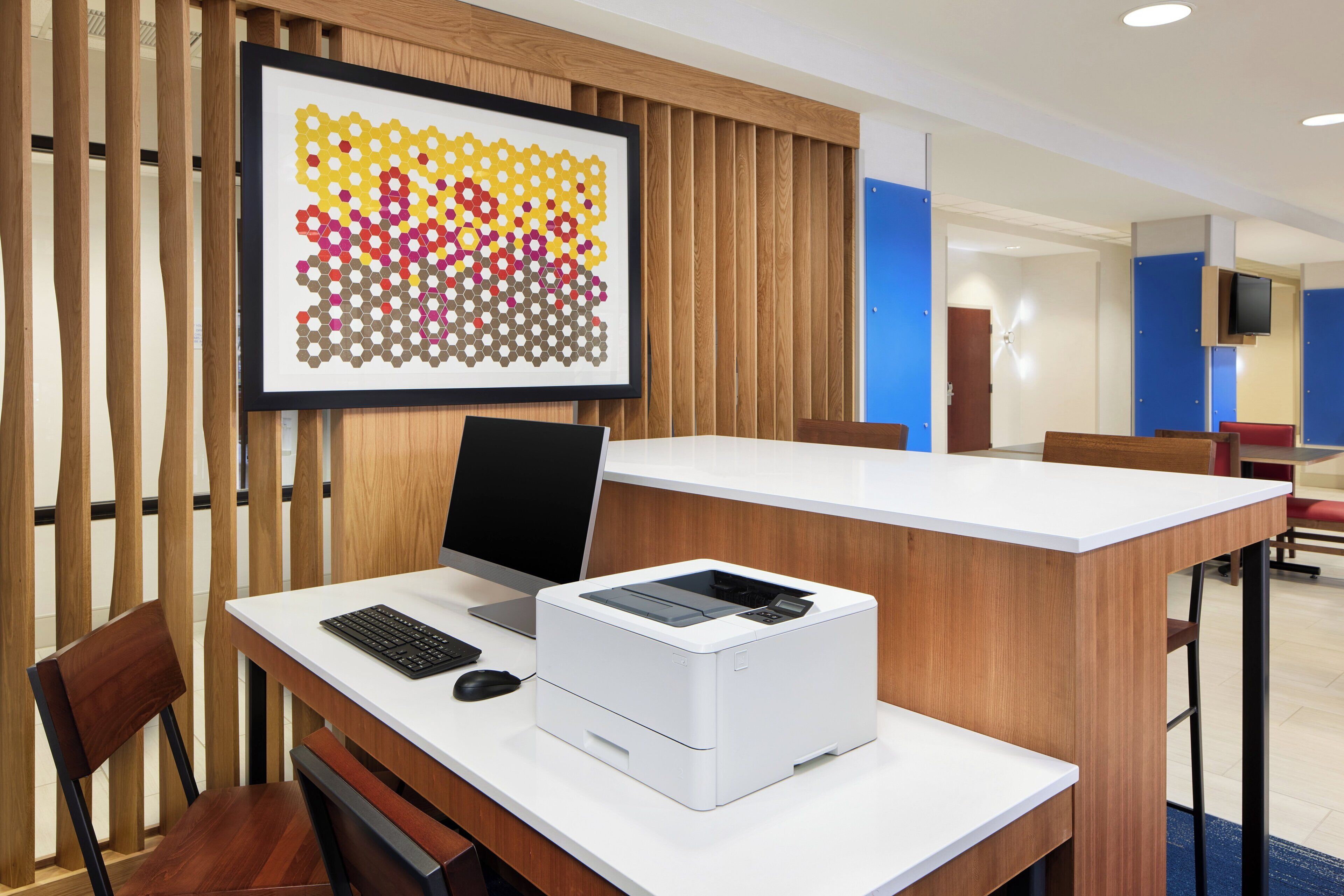 A modern office space with a desk, computer, printer, and a framed artwork on the wall.