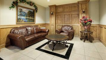 A room with a brown leather sofa, a matching armchair, a small round table, and a painting on the wall.