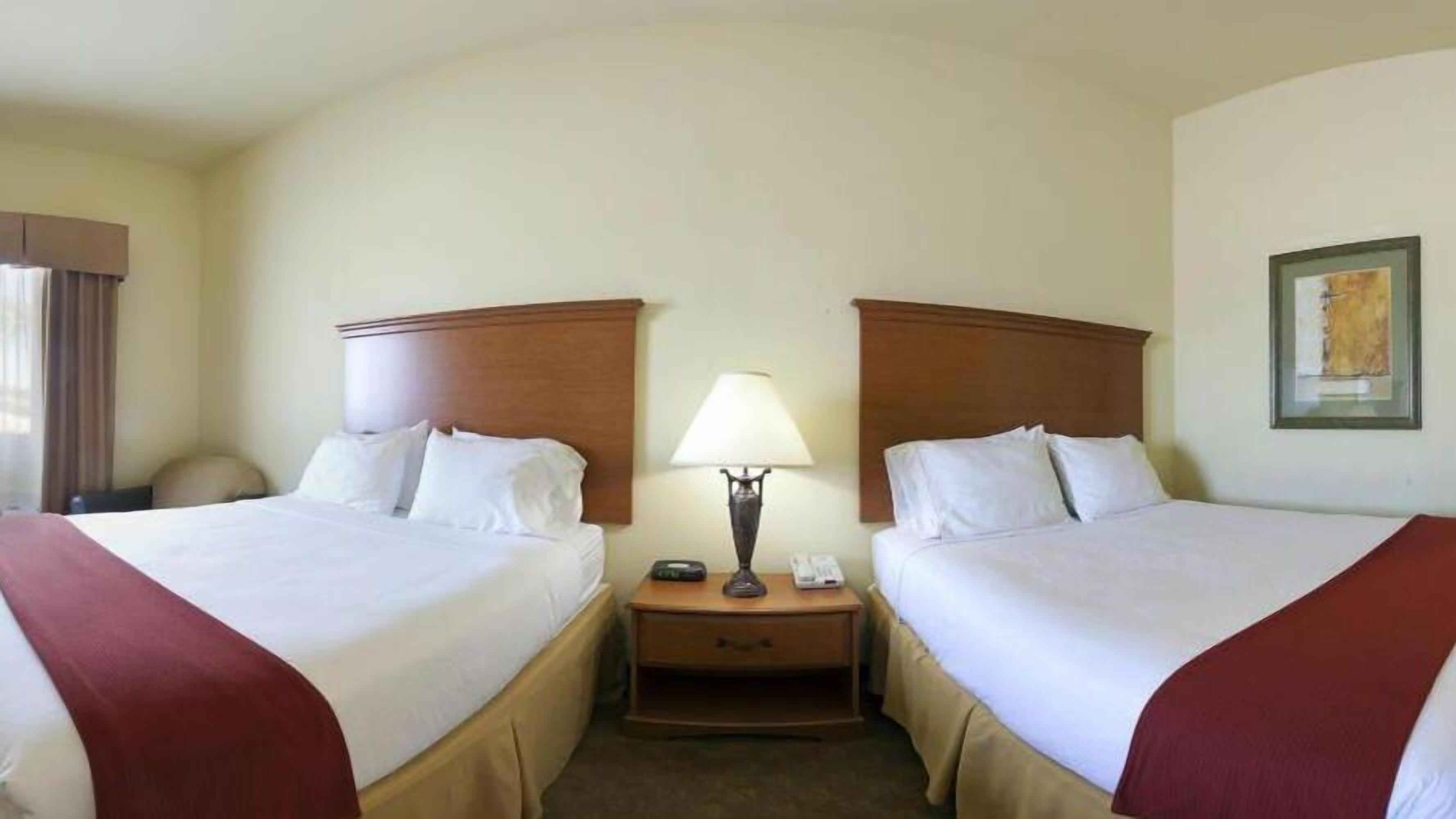 Habitación de hotel con dos camas, una mesita de noche con lámpara y un cuadro enmarcado en la pared.