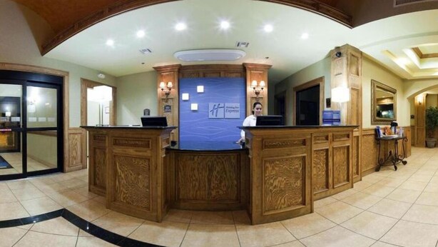 A reception desk with a blue backdrop and a logo, surrounded by wooden paneling and a tiled floor. - Holiday Inn Express & Suites Zapata by IHG (Zapata)