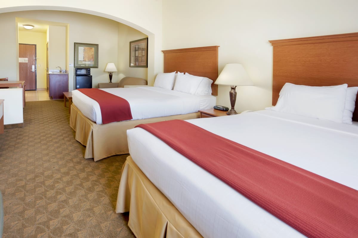 A hotel room with two beds, a desk, a chair, a microwave, and a small kitchenette.