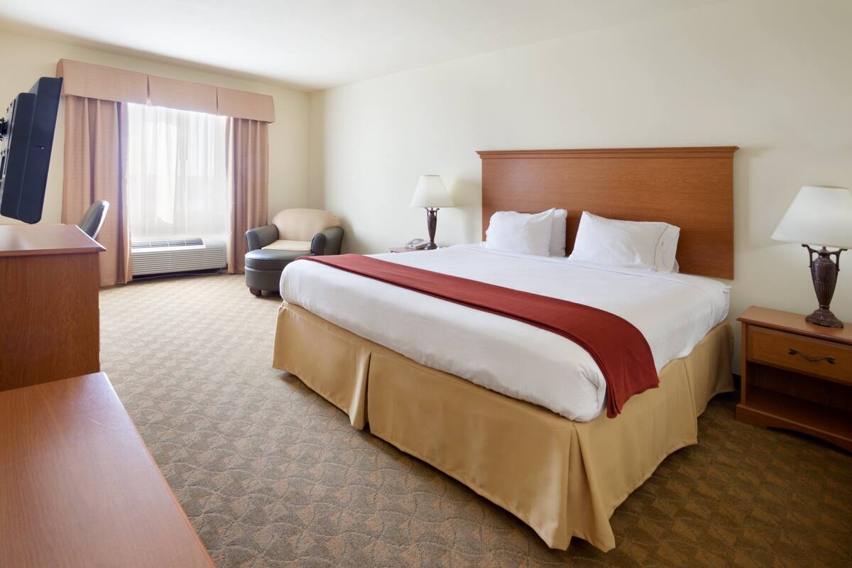 A hotel room with a large bed, a desk, a chair, a TV, and a window with curtains.