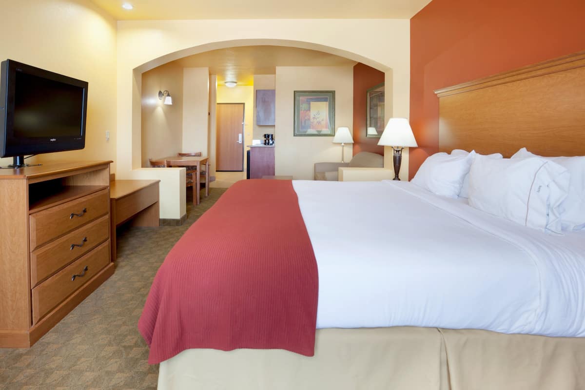 A hotel room with a large bed, a television, a desk, and a kitchenette.