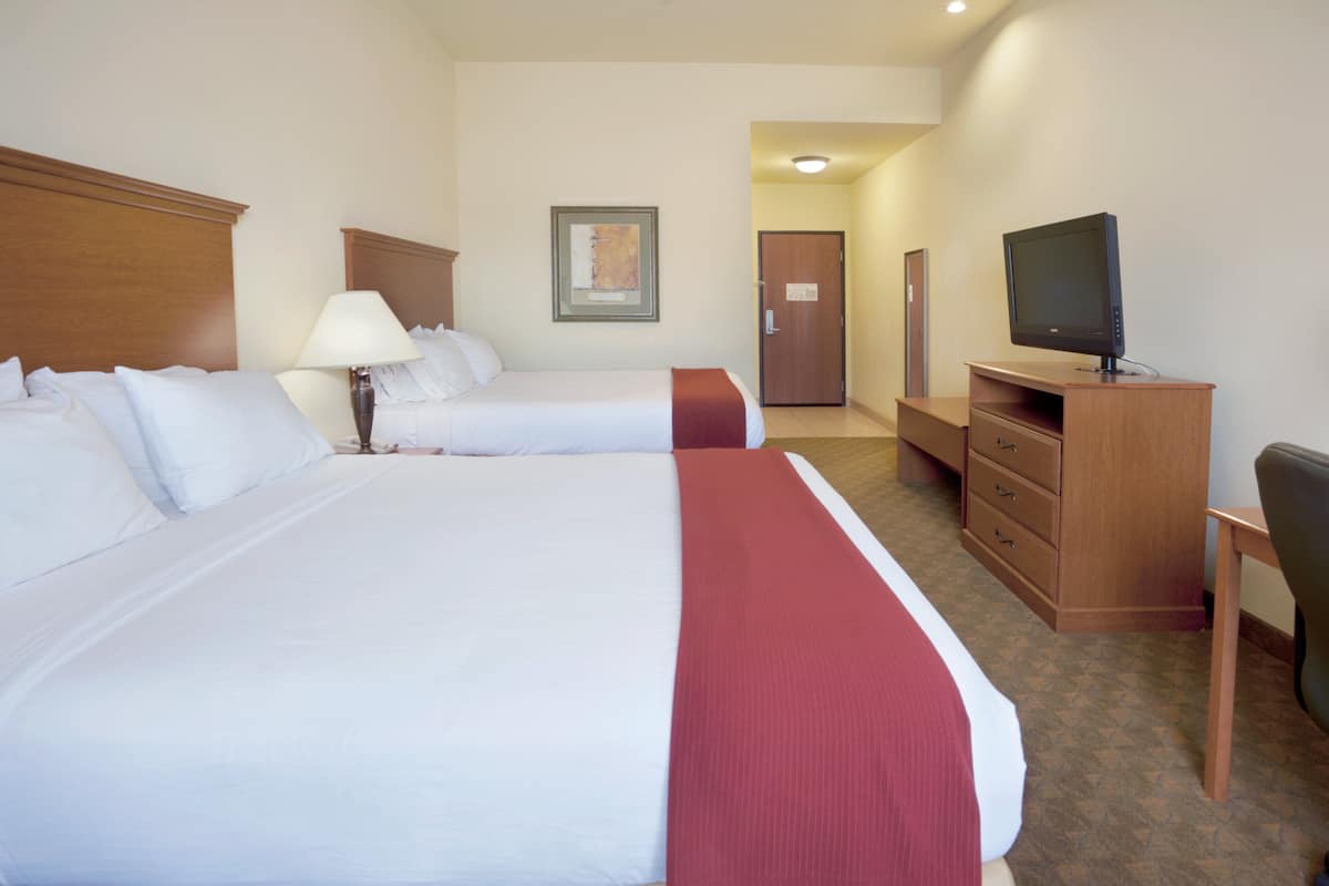 A hotel room with two beds, a desk, a television, and a door.