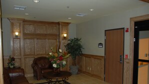 A lobby with a wooden panel wall, a leather sofa, a coffee table with flowers, and a door labeled "ROOOM". - Holiday Inn Express & Suites Zapata by IHG (Zapata)