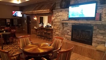 A cozy lounge area with a stone fireplace, a round wooden table, and striped chairs.