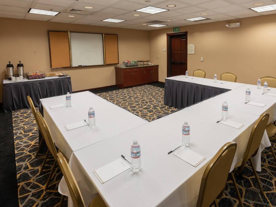 Sala de conferência com uma mesa comprida, cadeiras, tela de projetor e mesa de buffet com comida e bebida.