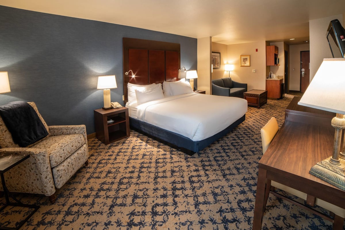 A hotel room with a large bed, a desk, a chair, a nightstand, and a lamp.