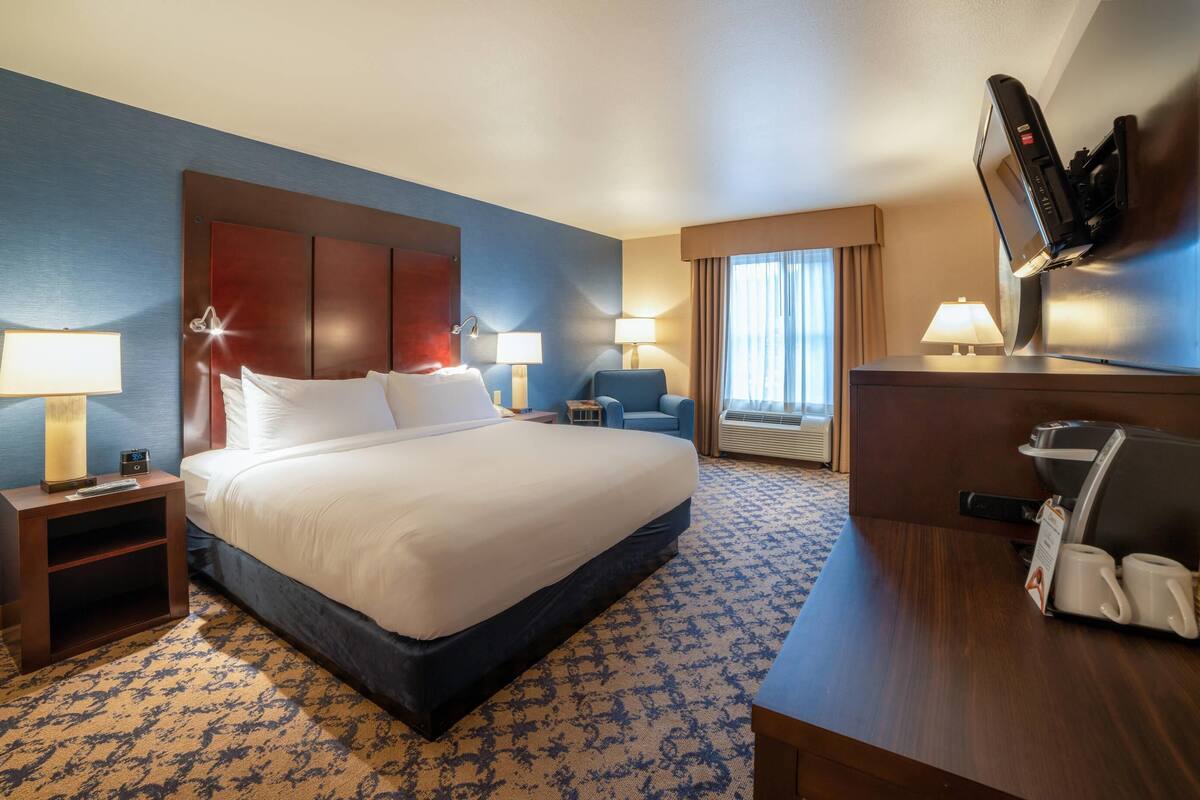 A hotel room with a large bed, two bedside tables with lamps, a desk with a coffee maker, and a flat-screen TV mounted on the wall.
