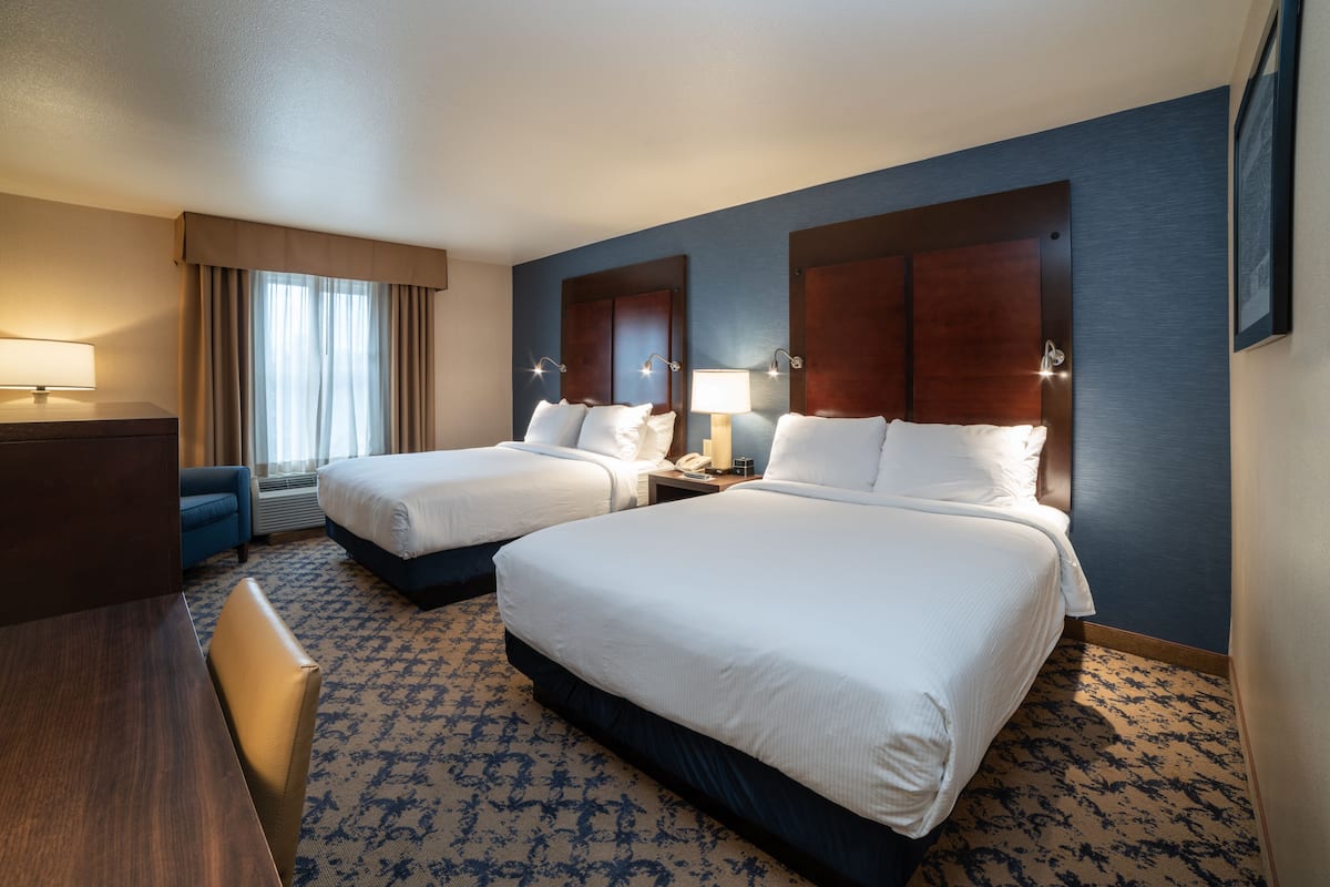 A hotel room with two beds, a desk, a chair, a lamp, and a window with curtains.