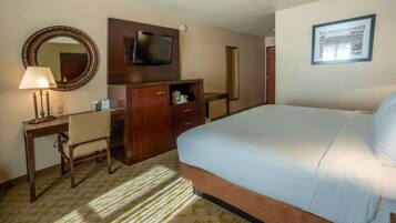 A hotel room with a bed, a desk, a chair, a TV, a mirror, and a framed picture on the wall.