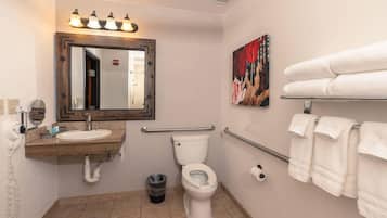 Un baño con lavamanos, espejo, inodoro y barras de apoyo.
