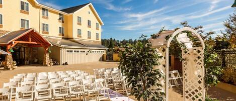 Decoración de boda con sillas blancas y un arco blanco en un espacio al aire libre, con un edificio al fondo.