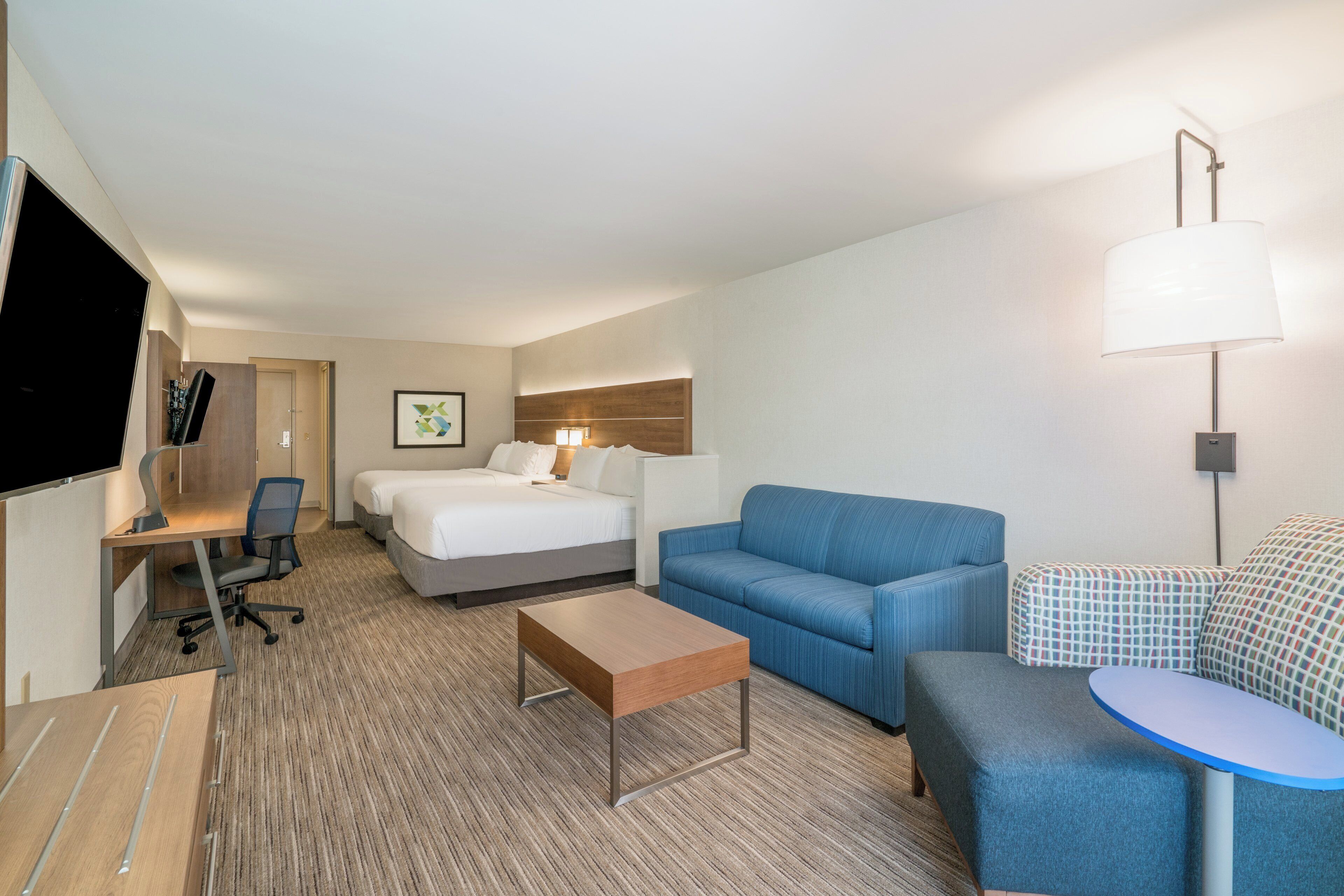 Une chambre d’hôtel comprenant un lit, un canapé, un bureau avec une chaise, une petite table et un téléviseur.