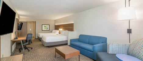 Une chambre d’hôtel comprenant un lit, un canapé, un bureau avec une chaise, une petite table et un téléviseur.
