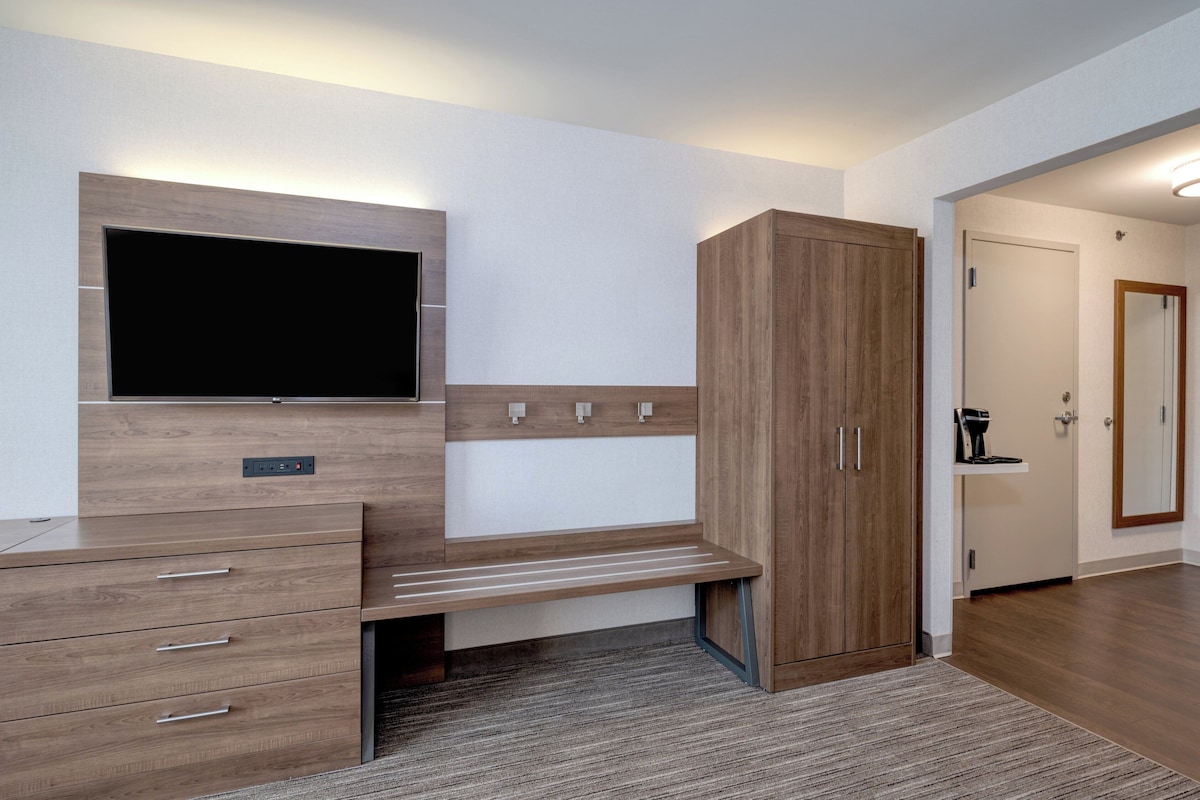 A modern room with a built-in TV, a wooden wardrobe, a desk with drawers, and a carpeted floor.