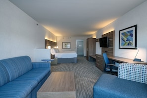 A hotel room with a bed, a sofa, a desk, and a TV.
