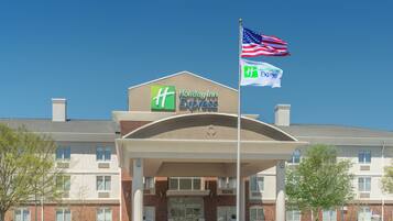 Un hotel Holiday Inn Express con fachada de ladrillo, un acceso cubierto y una bandera estadounidense.
