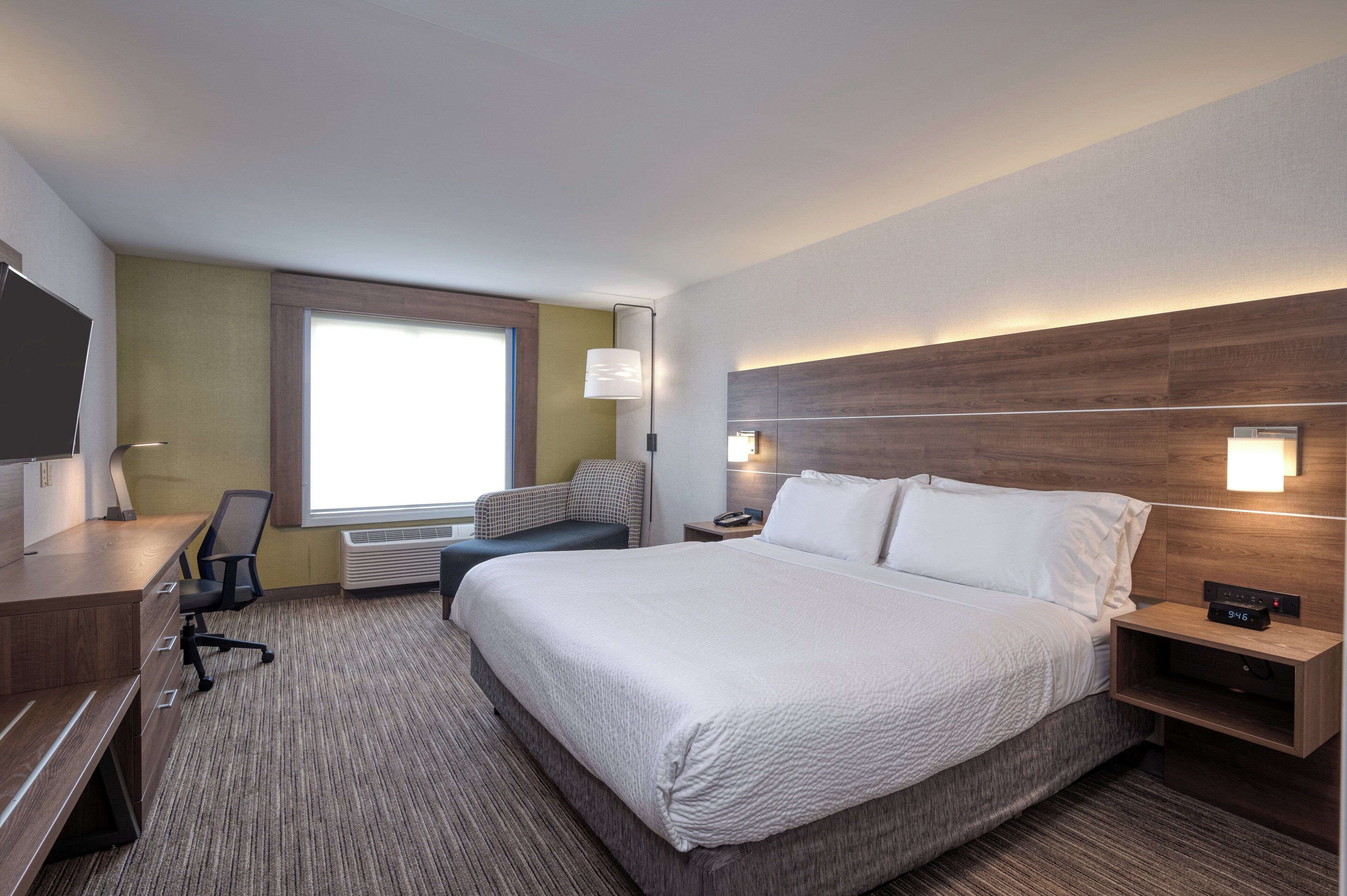 A hotel room with a large bed, a desk, a chair, a TV, and a window.
