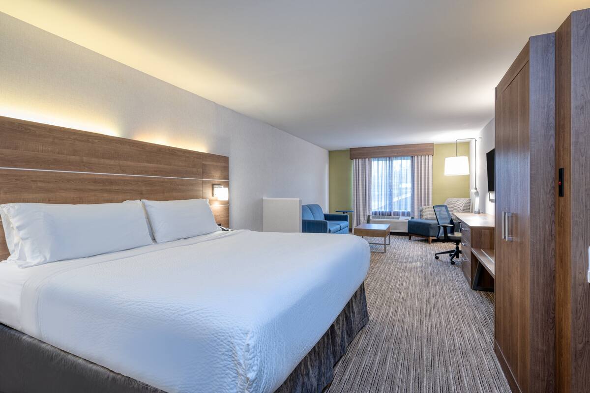 A hotel room with a large bed, a desk, a chair, and a TV.