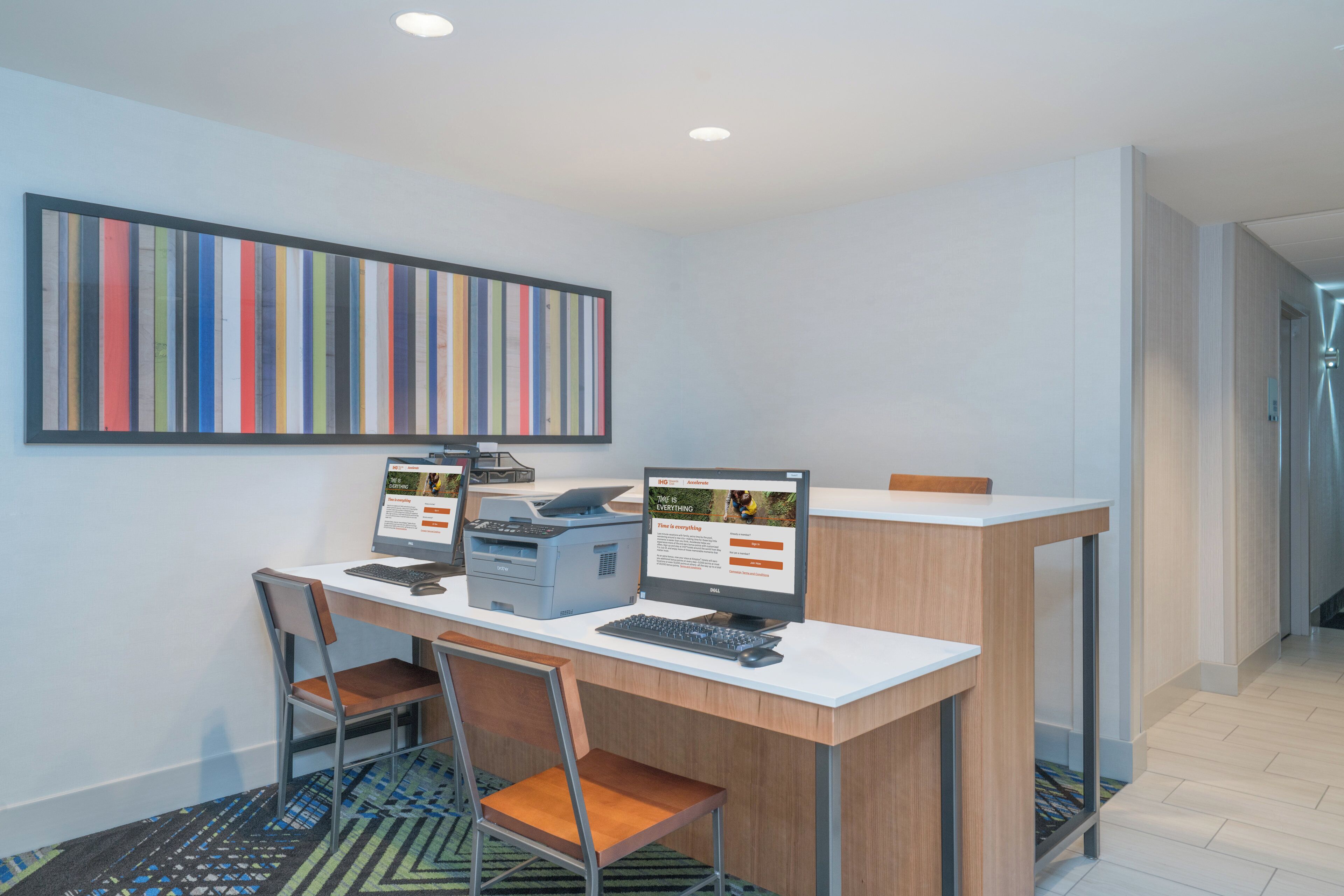 A modern office space with two desktop computers, a printer, and a large striped artwork on the wall.