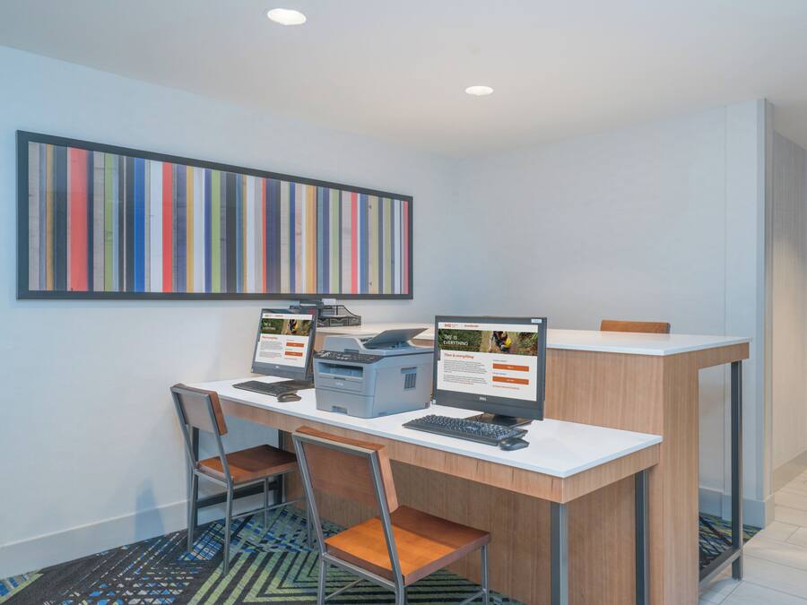 A modern office space with two desktop computers, a printer, and a large striped artwork on the wall.