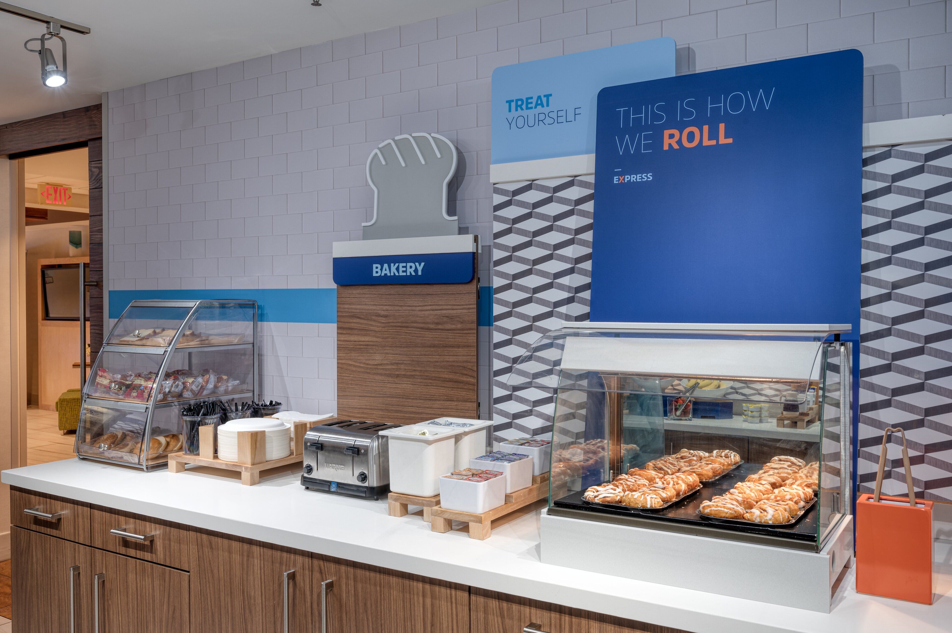 A bakery counter with a sign that reads "TREAT YOURSELF" and "THIS IS HOW WE ROLL."