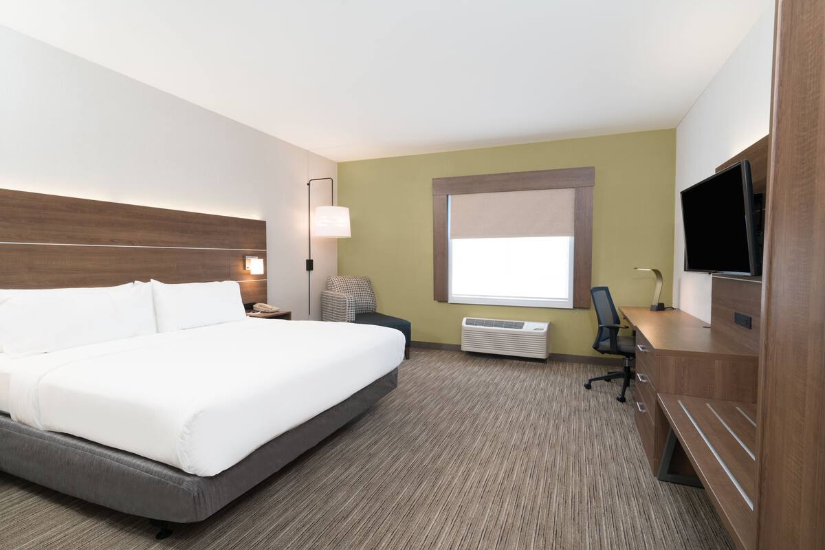 A hotel room with a large bed, a desk with a chair, a television, and a window with blinds.