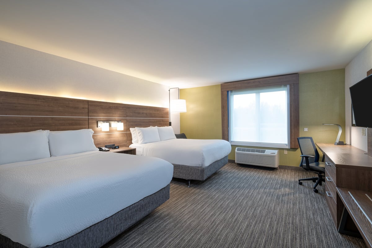 A hotel room with two beds, a desk, a chair, a TV, and a large window.