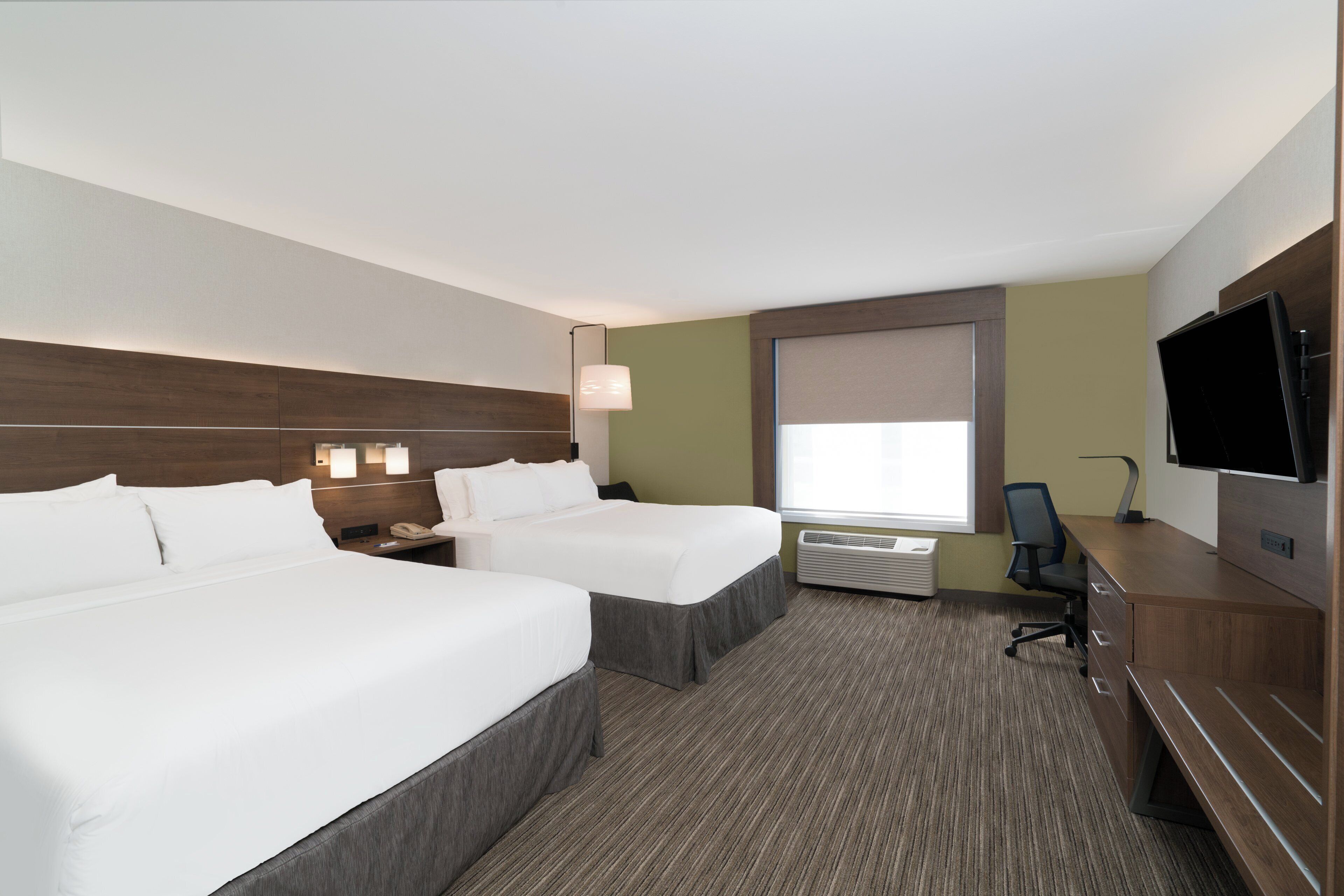 A hotel room with two beds, a desk, a television, and a window with blinds.