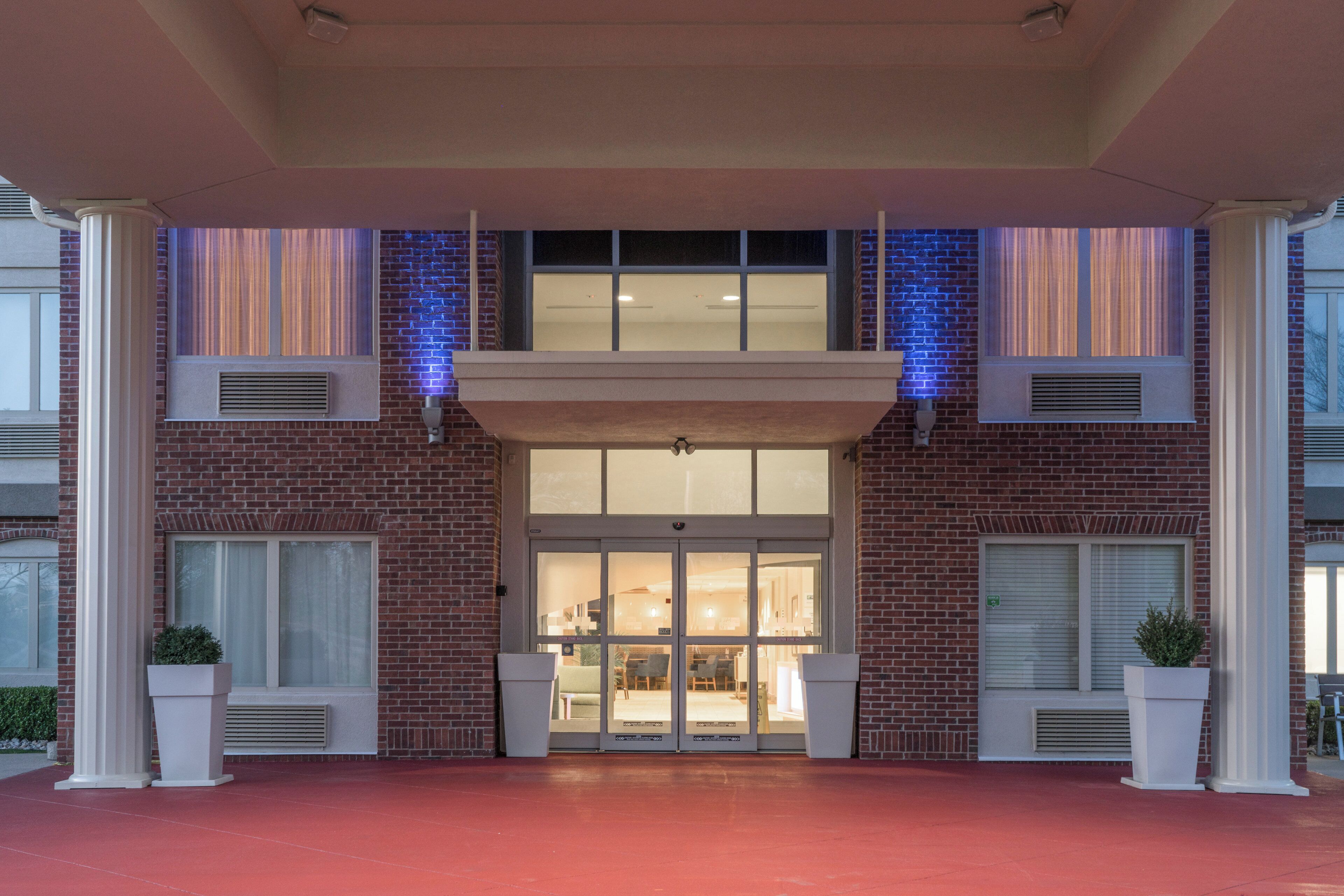 A hotel entrance with a brick facade, large windows, and a covered entrance area.