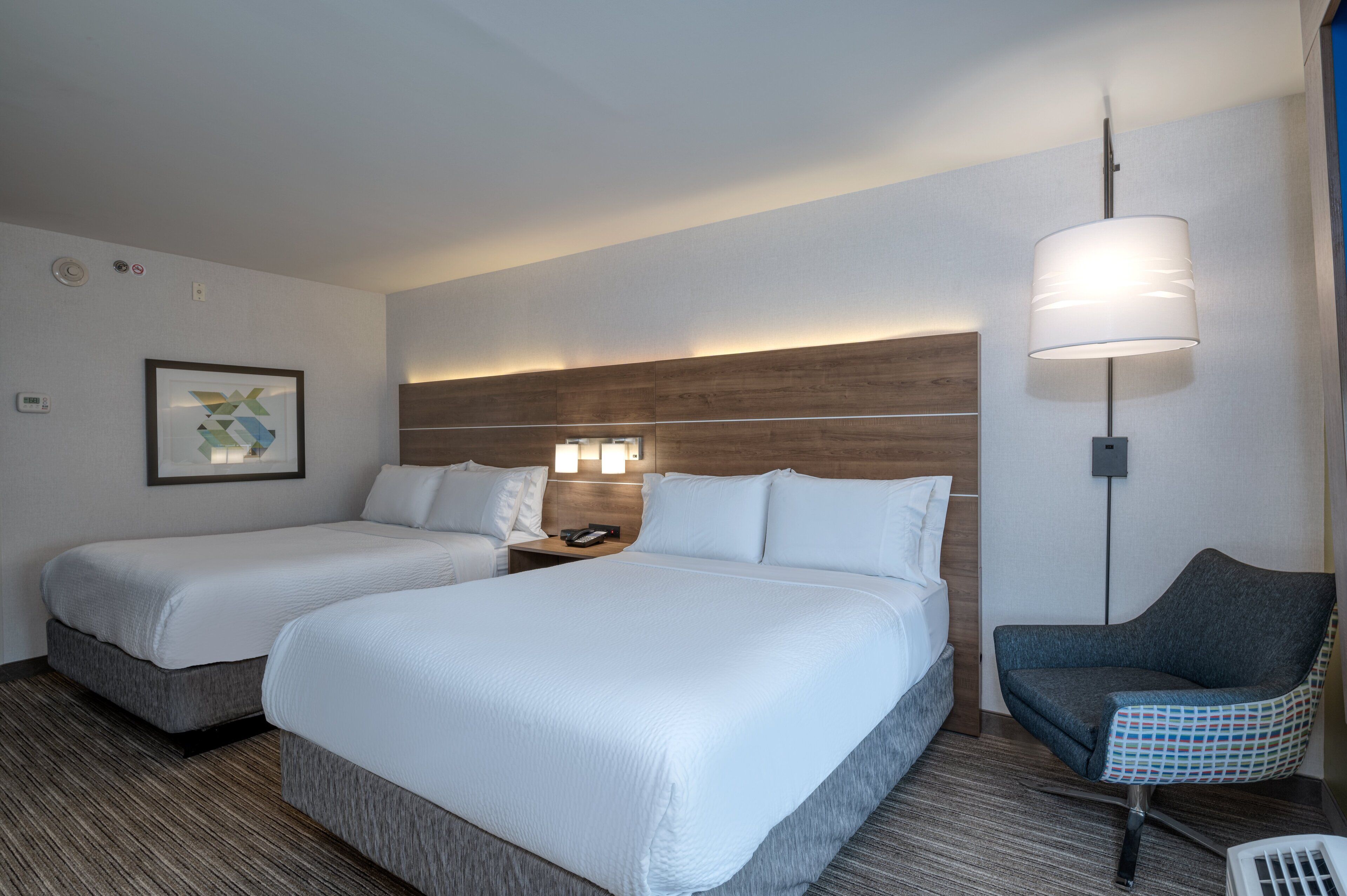 A hotel room with two beds, a desk, a chair, a lamp, and a framed picture on the wall.
