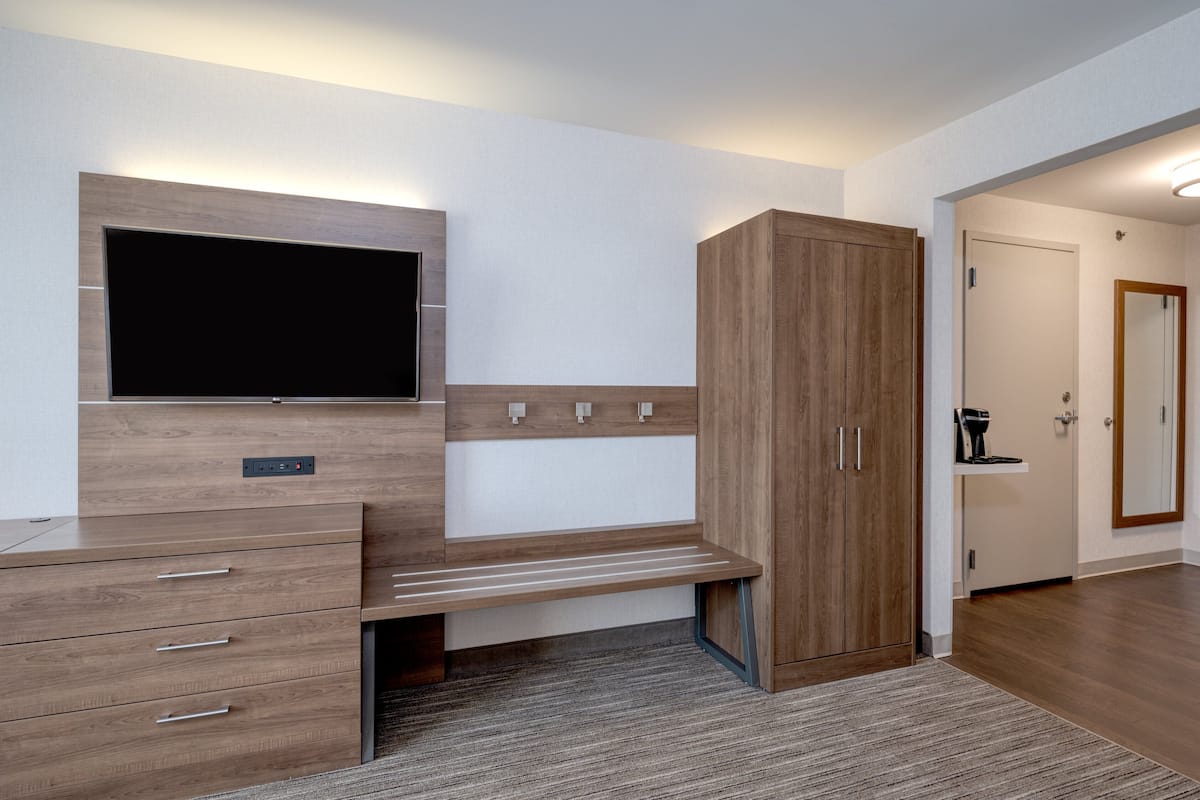 Habitació moderna amb escriptori de fusta, televisió plana penjada a la paret, armari i mirall.