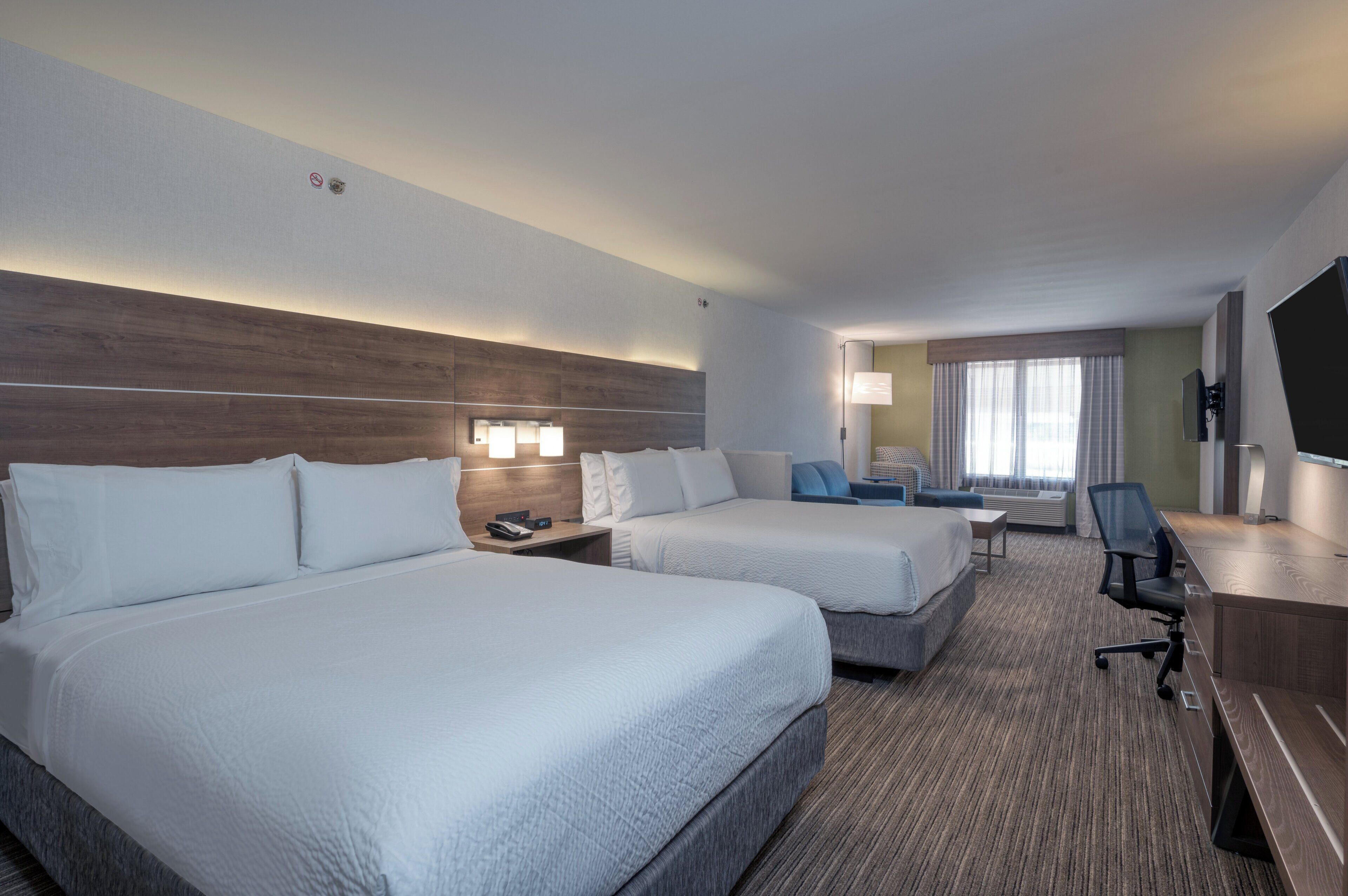 A hotel room with two beds, a desk, a chair, a TV, and a window with curtains.